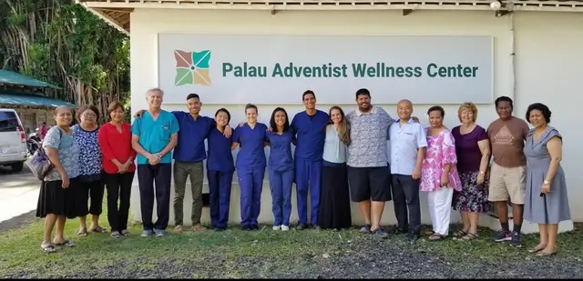 Clinic staff and volunteers in front of the Palau Adventist Wellness Center sign