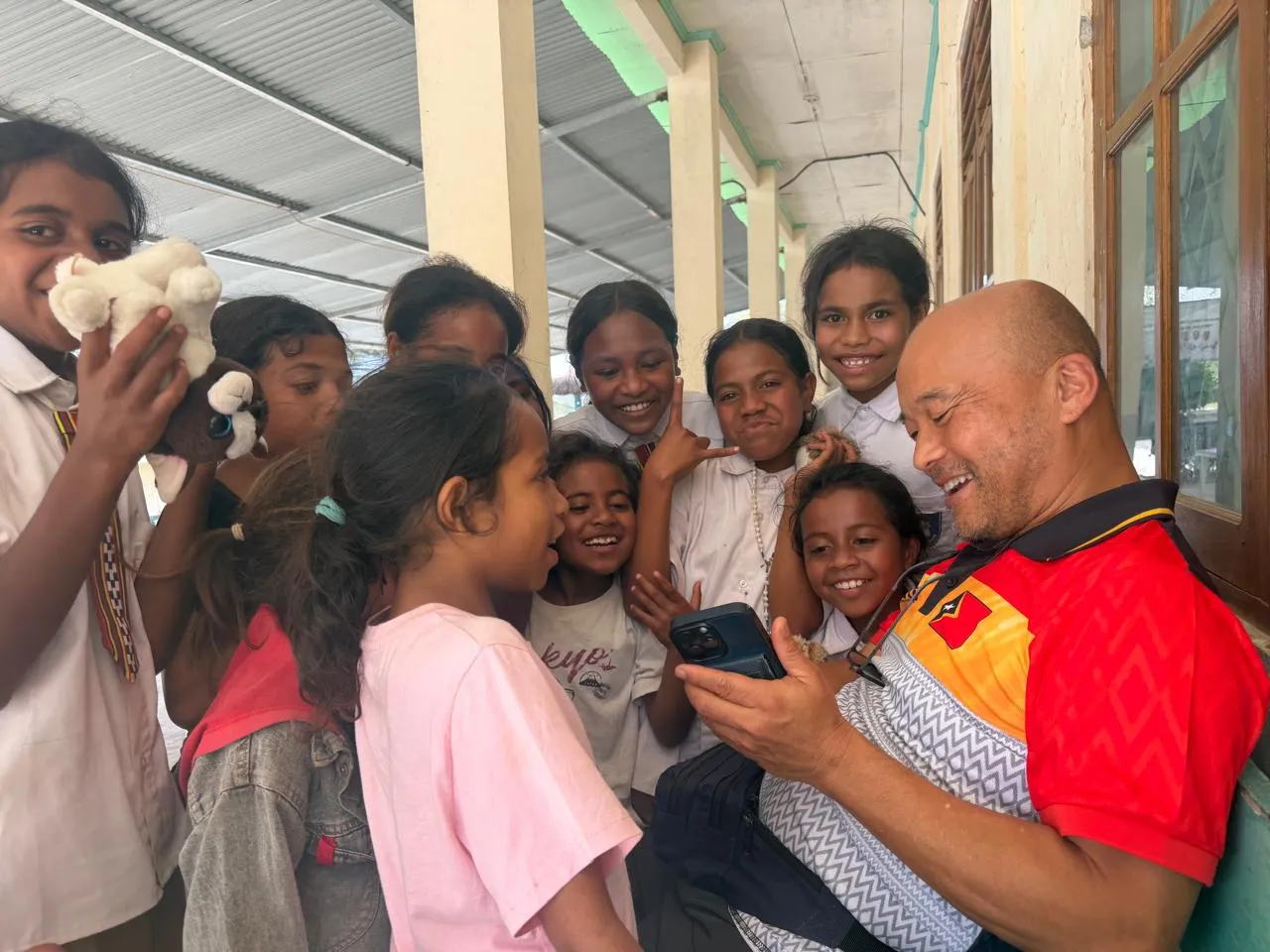Dr. Steve Chang showing his phone to a crowd of laughing children from Timor-Leste