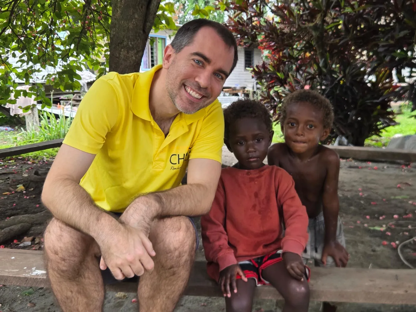 Tom sitting on a bench beside two young children from the Solomon Islands