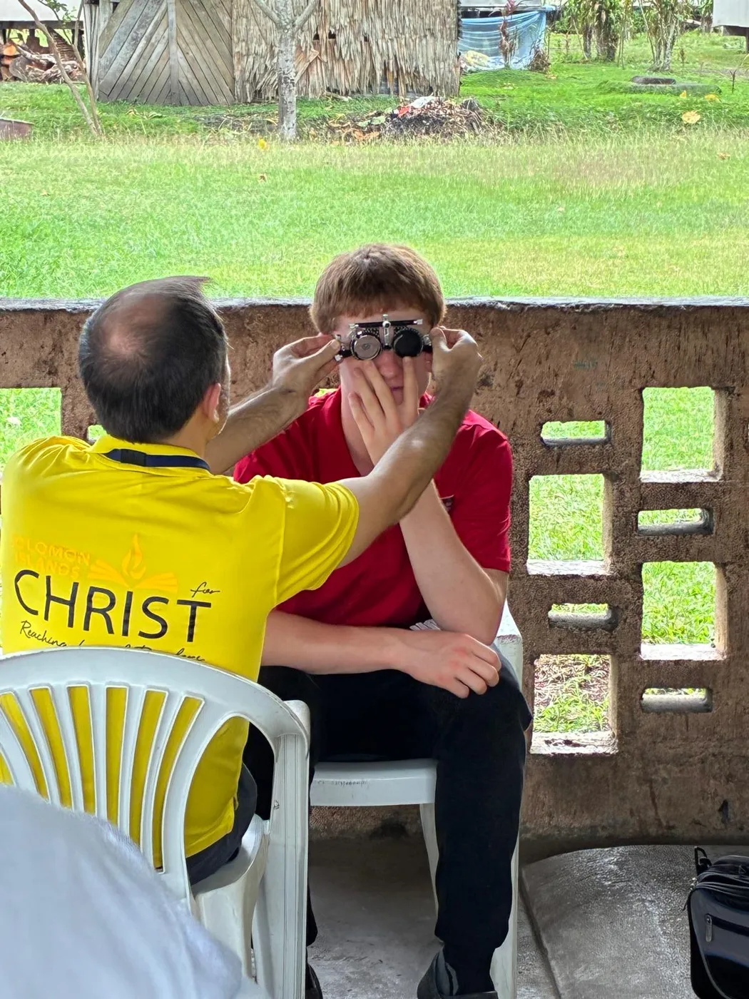 Tom in a yellow shirt holding a trial frame up to a patient during an eye test